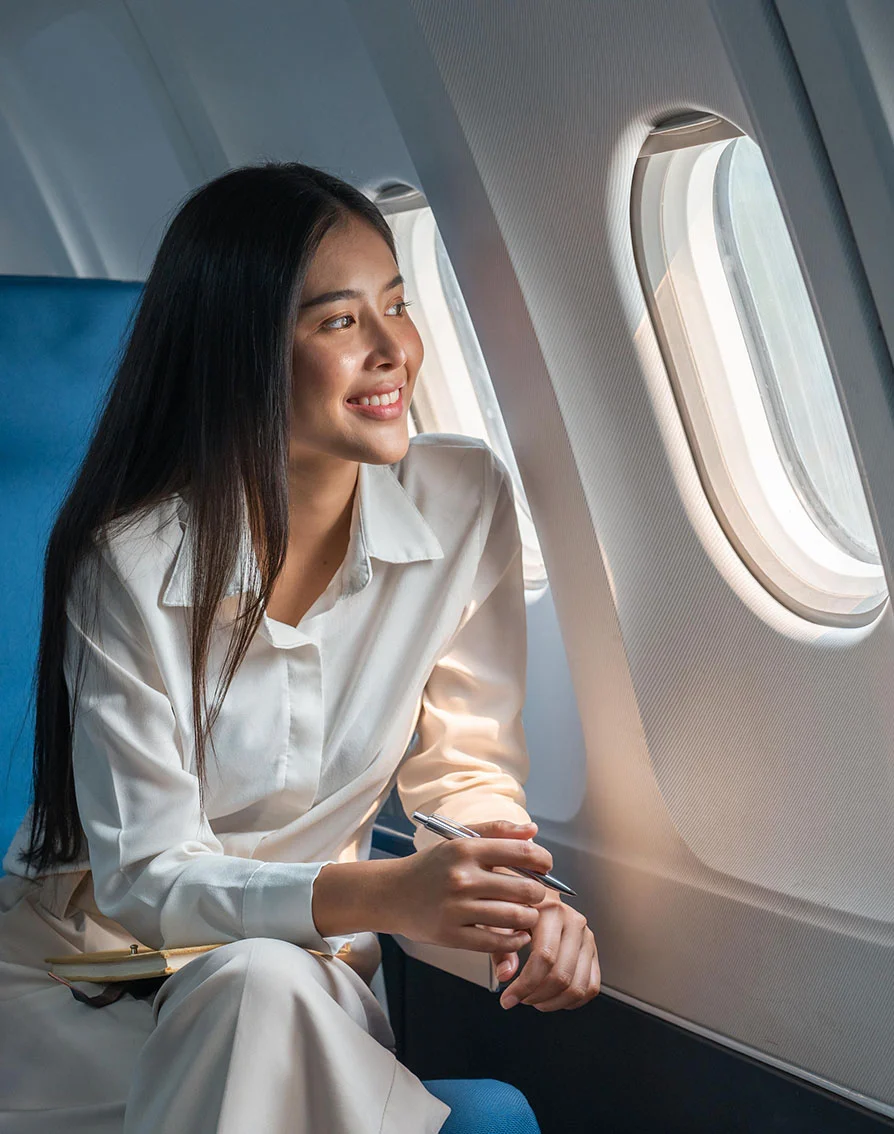 A woman sits in an airplane seat looking out the window smiling. Showing that she is happy to be where she is. - Out of Town in Folsom, CA